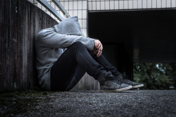 Depression, social isolation, loneliness, mental health and discrimination concept. Sad, lonely, depressed and unhappy man. Hooded person sitting in dark alley.